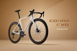 White bicycle with black details on a beige background, featuring 'Cobra Evo Gusto' branding.